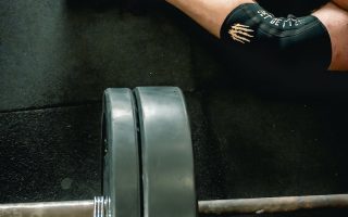 Person in Black Shoes Sitting Beside Barbell